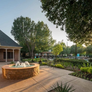 Sun peeking through the trees in a courtyard with a fountain at Villas of Spring Creek