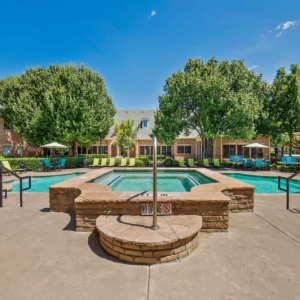 Alternate view of hot tub and pool with clubhouse and brightly colored lounge furniture in the background